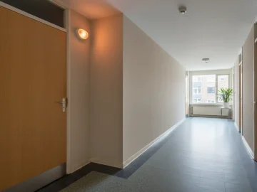 Editorial visual about realistic fire-safety stock photo in a Dutch apartment corridor: smoke detector on ceiling