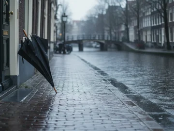 Editorial visual about realistic Dutch weather stock photo with rain on canal-side pavement, umbrella leaning nea