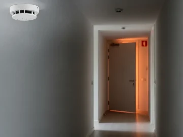 News image about realistic fire-safety stock photo in a Dutch apartment corridor: smoke detector on ceiling
