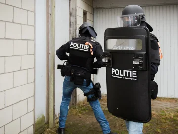 Two FIOD Team Bijzondere Bijstand officers with a POLITIE shield entering a building during a search