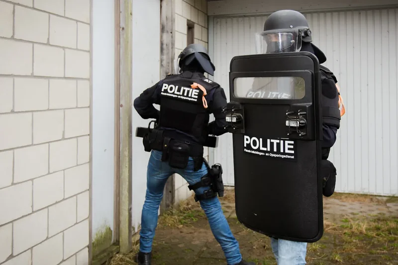 Two FIOD Team Bijzondere Bijstand officers with a POLITIE shield entering a building during a search