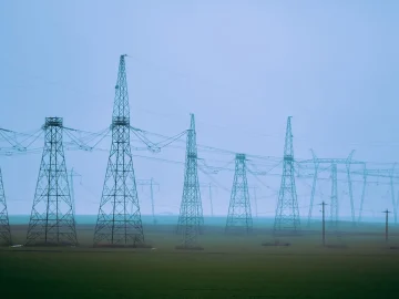 Rows of high-voltage electricity pylons crossing flat farmland in mist