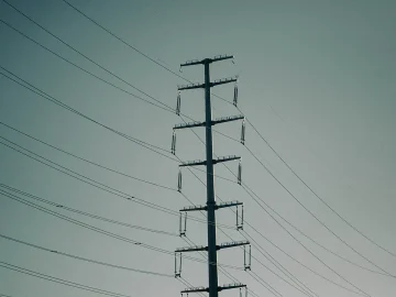 A line of high-voltage electricity pylons silhouetted against an evening sky