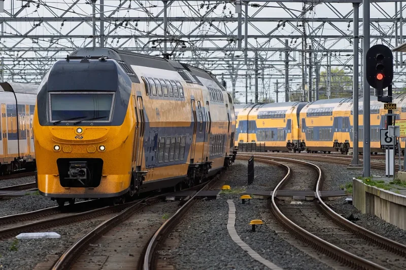 Yellow and blue NS intercity trains standing still at a Dutch railway yard beside a red signal