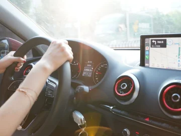 Driver's hands on the steering wheel, with a navigation map on the dashboard screen