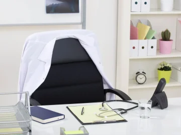 Empty medical office with a desk, stethoscope and a white coat over the chair