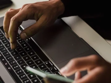 Hands typing on a laptop while holding a smartphone