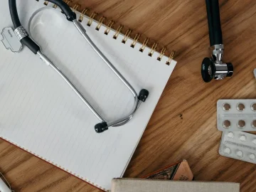Stethoscope, notebook, glasses and blister packs of tablets on a wooden desk